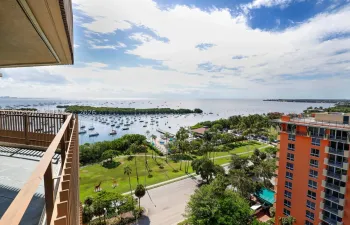 Elevated outdoor balcony with metal railing, overlooking a coastal expanse, harbor, and landscaped green space