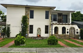 Two-story exterior featuring a stone-clad facade, arched entryway detailing, a covered second-story balcony with metal railing, and a pergola-style overhang