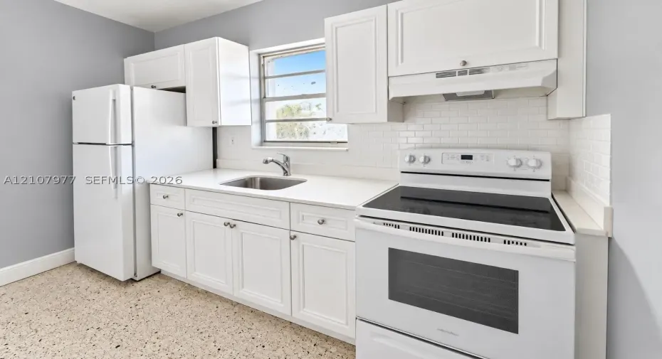 Kitchen featuring white shaker-style cabinetry, solid-surface countertops, a subway tile backsplash, terrazzo flooring, and stainless steel undermount sink