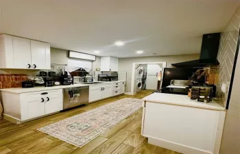 Main House Kitchen featuring white cabinetry, wood-finish flooring, a herringbone-patterned tile backsplash, a black range hood, and stainless steel appliances