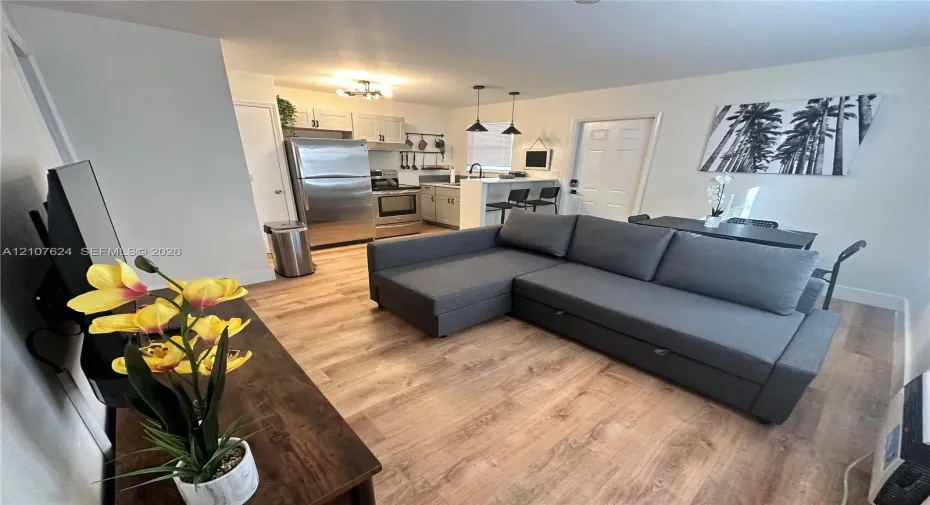 Open-concept kitchen featuring wood-finish flooring, stainless steel appliances, neutral cabinetry, and a breakfast bar illuminated by pendant lighting