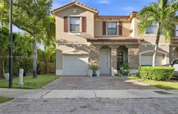 Two-story stucco exterior featuring a stone-veneer entryway, tiled roof, decorative shutters, and a paved driveway