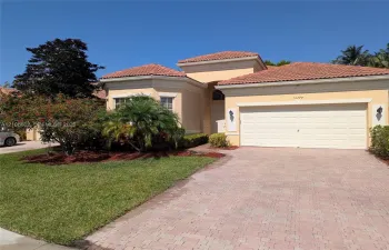 Stucco exterior featuring a multi-gabled tile roof, paver driveway, attached two-car garage, and landscaped front garden