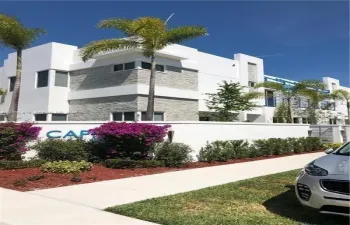 Contemporary multi-level exterior featuring white smooth-stucco finish, stacked-stone masonry detailing, flat roof lines, and perimeter privacy wall with professional landscaping
