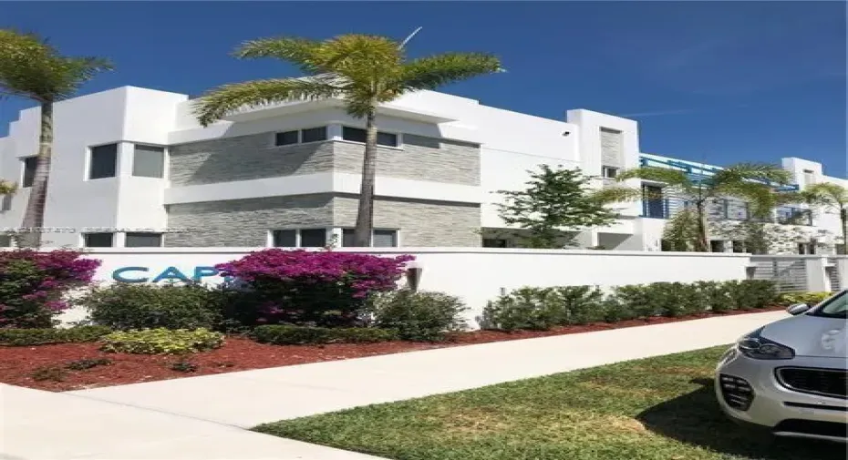 Contemporary multi-level exterior featuring white smooth-stucco finish, stacked-stone masonry detailing, flat roof lines, and perimeter privacy wall with professional landscaping