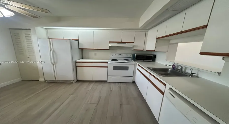 Kitchen featuring white cabinetry with wood trim, wood-finish flooring, integrated white appliances, and a stainless steel dual-basin sink