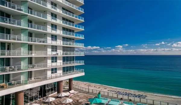 High-rise exterior featuring stacked cantilevered balconies with glass railings, full-height windows, and direct oceanfront positioning