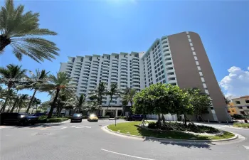 High-rise residential building featuring private balconies, expansive structural facade, and landscaped circular driveway with mature palm trees