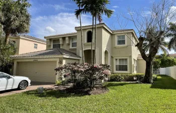 Two-story stucco exterior featuring a tiled roof, arched architectural details, a multi-car garage, and established palm trees