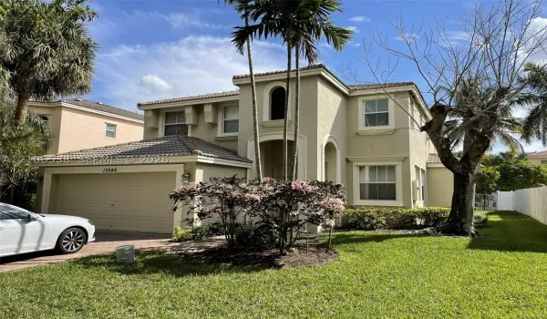 Two-story stucco exterior featuring a tiled roof, arched architectural details, a multi-car garage, and established palm trees