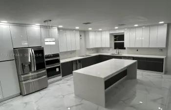 Kitchen featuring high-gloss white upper cabinetry, dark lower cabinetry, a large central island with a stone-finish waterfall countertop, stainless steel appliances, and large-format tile flooring