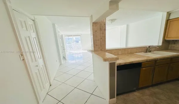 Kitchen featuring tile countertops, mosaic tile backsplash, wood-finish cabinetry, a built-in dishwasher, and white ceramic tile flooring