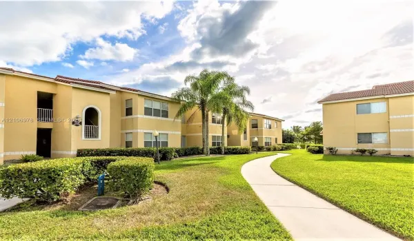 Multi-story stucco exterior featuring tile roofing, arched balcony detailing, manicured landscaping, and concrete walkways