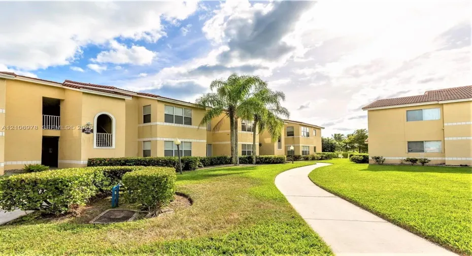 Multi-story stucco exterior featuring tile roofing, arched balcony detailing, manicured landscaping, and concrete walkways