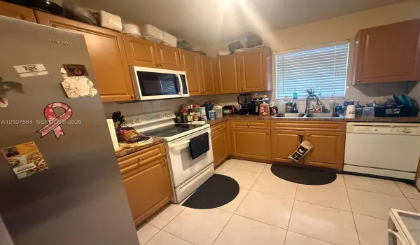 Kitchen featuring wood cabinetry, tile flooring, stainless steel refrigerator, white appliance package, and double basin sink