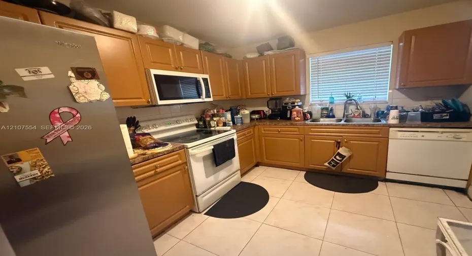 Kitchen featuring wood cabinetry, tile flooring, stainless steel refrigerator, white appliance package, and double basin sink