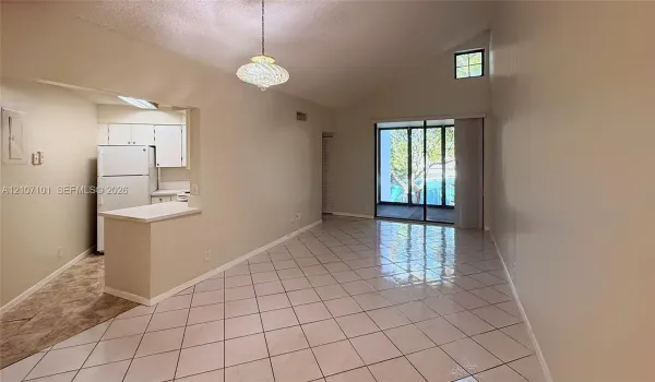 Vaulted ceilings featuring a glass pendant fixture, neutral tile flooring, kitchen with breakfast bar, and sliding glass doors with overhead transom window