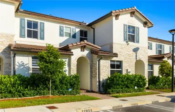 Stucco exterior featuring stacked stone accents, decorative shutters, clay tile roof detailing, and arched entryway