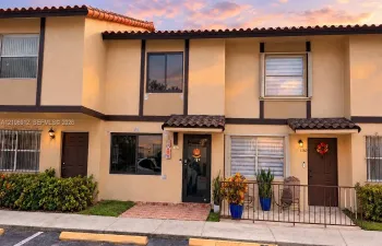 Two-story stucco exterior featuring a tiled roof, dark-framed windows, brick-paved entryway, and metal exterior railings