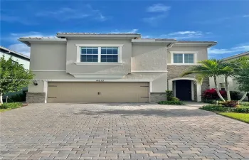 Two-story exterior featuring a paver driveway, stone facade detailing, multi-pane windows, and an attached multi-car garage