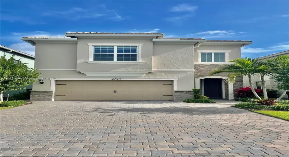 Two-story exterior featuring a paver driveway, stone facade detailing, multi-pane windows, and an attached multi-car garage