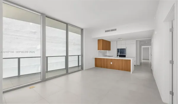Floor-to-ceiling windows, porcelain tile flooring, kitchen with wood-finish cabinetry, white slab countertops, and an integrated glass balcony railing
