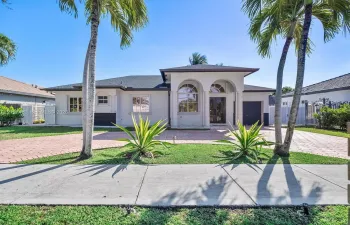 Stucco exterior featuring dual arched entryways, a paved driveway, decorative stone-trimmed windows, and mature palm landscaping