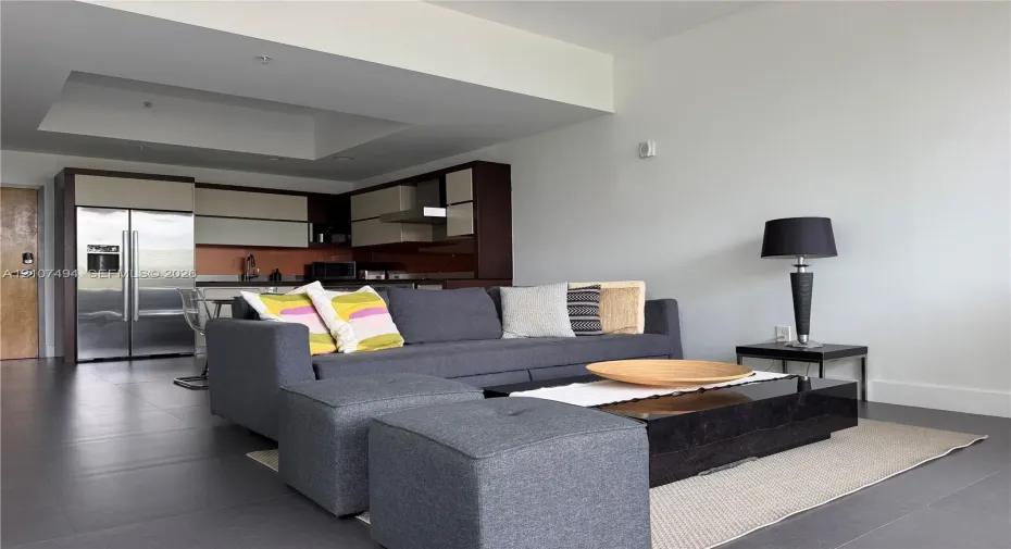 Open-concept area featuring oversized neutral floor tiling, recessed ceiling detail, and kitchen cabinetry with a two-tone finish
