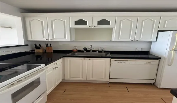 Kitchen featuring white cabinetry with glass-panel accents, dark countertops, a stainless steel undermount sink, and wood-finish flooring