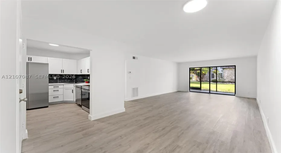 Kitchen featuring white shaker cabinetry, stainless steel appliances, and dark tile backsplash, complemented by wood-finish flooring and floor-to-ceiling glass sliding doors