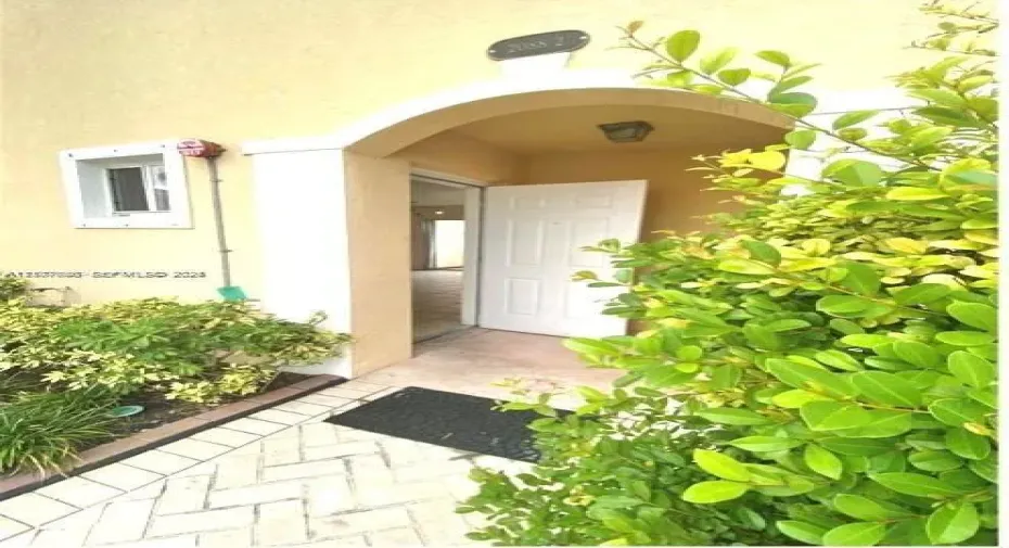 Covered entryway featuring a stucco archway, herringbone-patterned paved walkway, and built-in exterior lighting