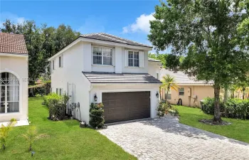 Two-story exterior featuring a light-toned stucco facade, a dark-toned tile roof, a paver driveway, and an attached two-car garage