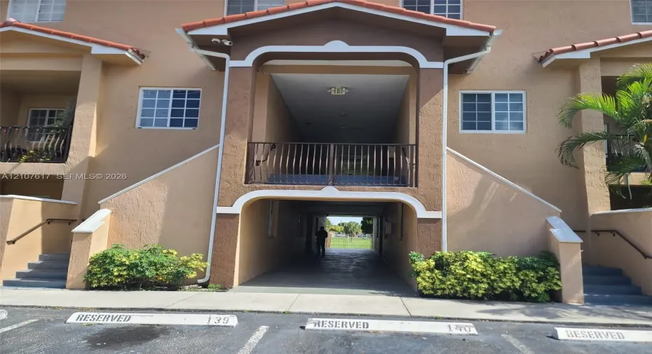 Stucco exterior with an arched entryway, elevated balcony featuring metal railings, and two sets of concrete exterior stairs