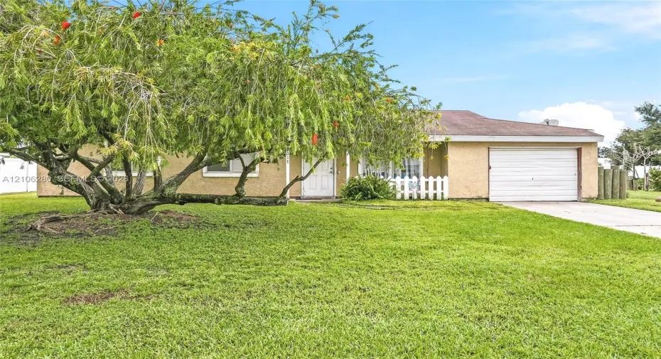 Stucco exterior featuring a concrete driveway, attached one-car garage, and picket fencing