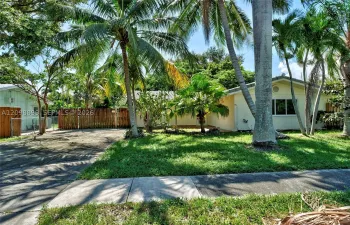 Exterior facade featuring light-toned siding, concrete driveway, wood privacy fencing, and mature palm trees