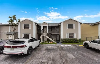Two-story exterior featuring a neutral stucco facade, white trim accents, gabled rooflines, designated parking spaces, and covered entryways