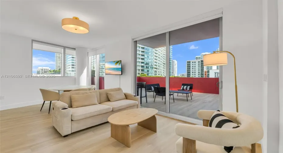 Living area featuring wood-finish flooring, floor-to-ceiling windows, and a sliding glass door providing access to a private balcony with wood-finish decking