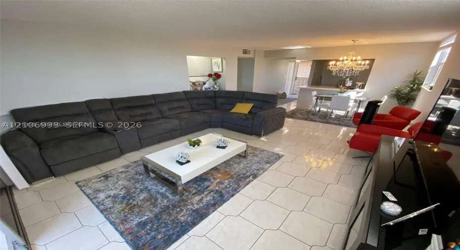 Open-concept interior featuring light-toned tile flooring, recessed ceiling lighting, and a chandelier-style fixture