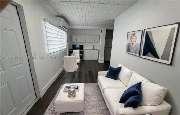 Plank-style flooring, white tongue-and-groove paneled ceiling, wall-mounted ductless heating and cooling unit, built-in white cabinetry with a sink, and window roller shades