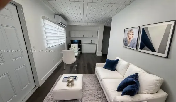 Plank-style flooring, white tongue-and-groove paneled ceiling, wall-mounted ductless heating and cooling unit, built-in white cabinetry with a sink, and window roller shades