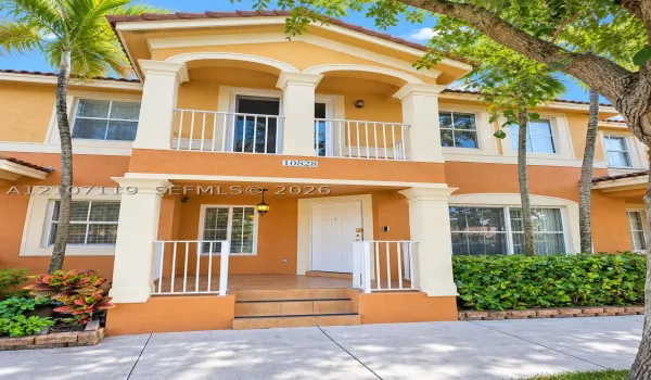 Stucco exterior featuring dual-level covered porches with white railing, decorative architectural columns, and tiled entry steps