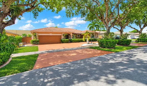 Single-story residence featuring a tiled roof, expansive paved driveway, multi-car garage, and established landscaping with mature trees