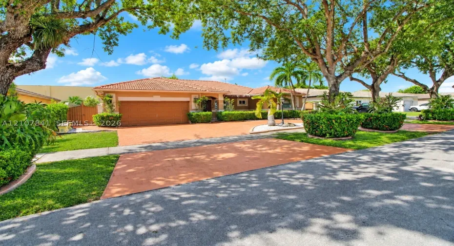 Single-story residence featuring a tiled roof, expansive paved driveway, multi-car garage, and established landscaping with mature trees