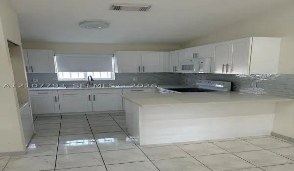 Kitchen featuring white shaker-style cabinetry, light-toned stone countertops, a mosaic tile backsplash, a peninsula, and tile flooring