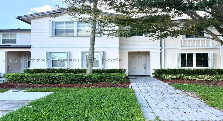 Two-story townhome exterior featuring horizontal lap siding, a paved stone walkway, multi-pane windows, and a built-in upper-level balcony with railings