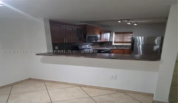 Kitchen featuring stained wood cabinetry, stone-patterned laminate countertops, stainless steel appliances, and ceramic tile flooring