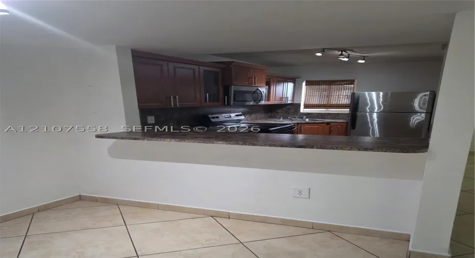 Kitchen featuring stained wood cabinetry, stone-patterned laminate countertops, stainless steel appliances, and ceramic tile flooring