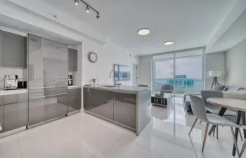 Modern kitchen featuring high-gloss cabinetry, a central island with a waterfall countertop, integrated stainless steel refrigerator, porcelain tile flooring, and floor-to-ceiling glass doors