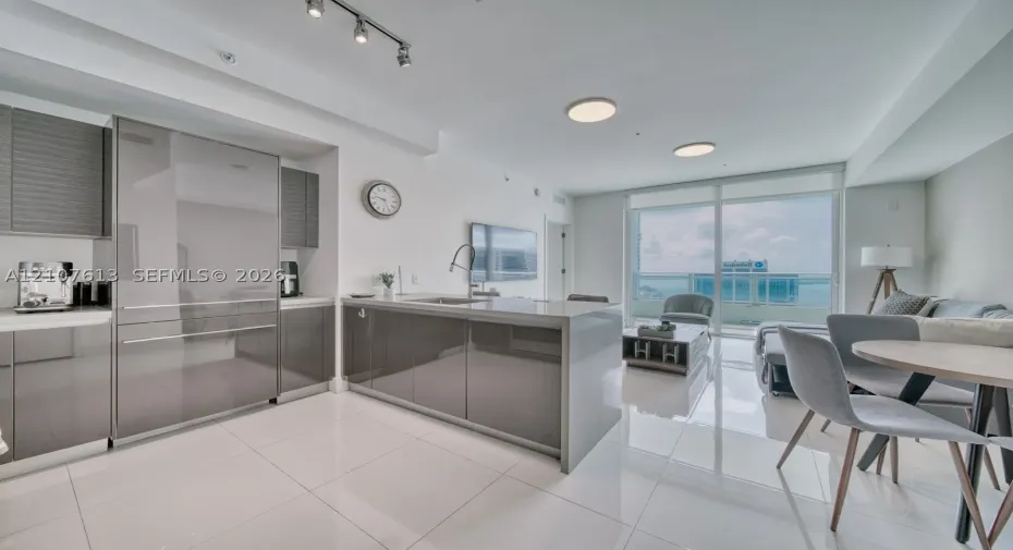 Modern kitchen featuring high-gloss cabinetry, a central island with a waterfall countertop, integrated stainless steel refrigerator, porcelain tile flooring, and floor-to-ceiling glass doors