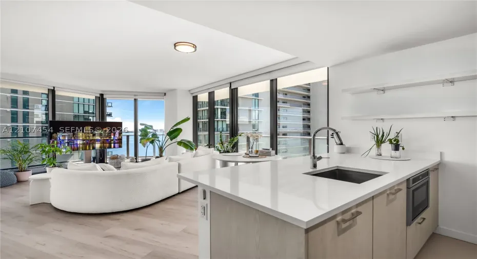 Kitchen featuring a white quartz countertop, undermount sink, gooseneck faucet, light-finish cabinetry, and built-in microwave, complemented by wood-finish flooring and floor-to-ceiling windows